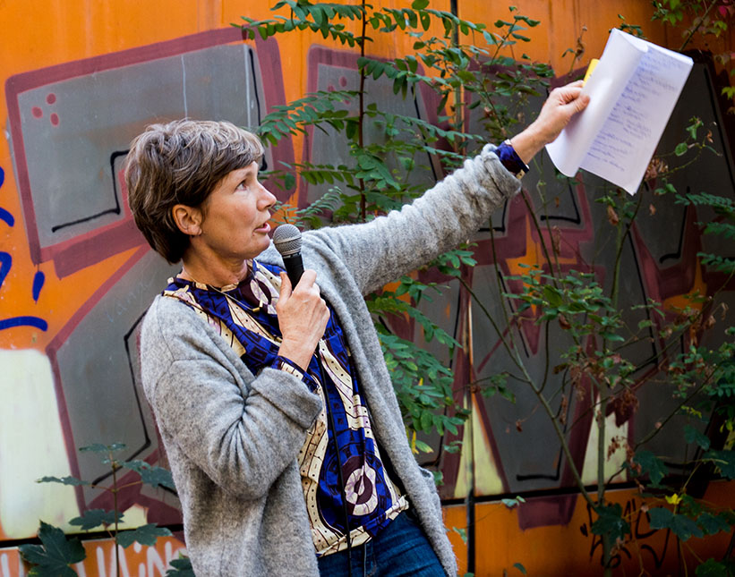 Foto: Frau am Mikrofon zeigt auf Schule