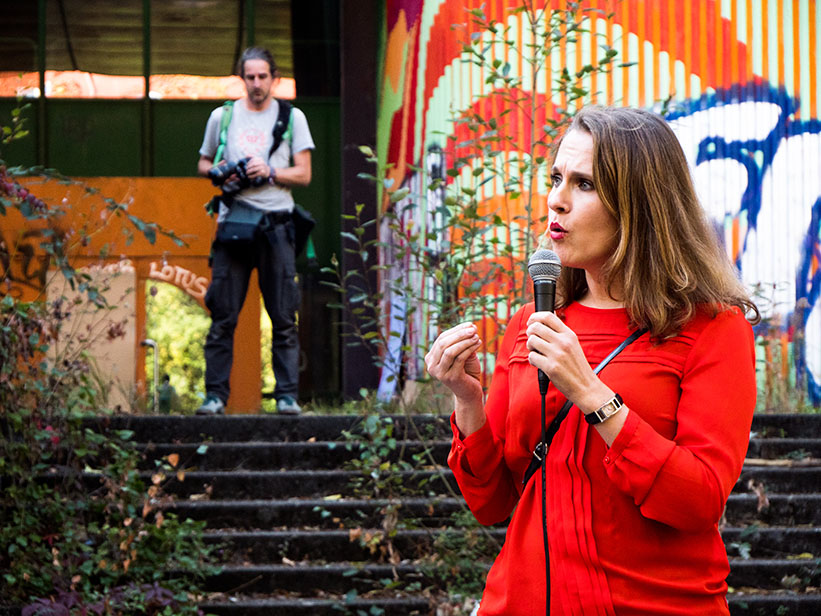 Foto: Frau am Mikrofon vor ehemaliger Schule