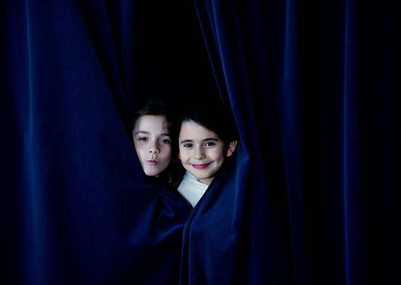 zwei Mädchen gucken zwischen Vorhang hervor
